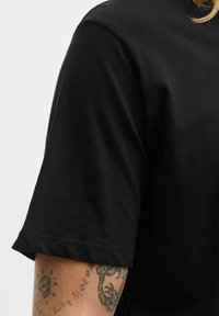 Sort bomulds T-shirt med rund hals og korte ærmer i en glat tekstur. Bemærkelsesværdig detalje inkluderer en stikning nær ærmet.