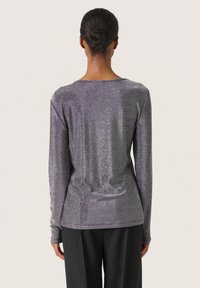 Garš sleeves tops ar spīdīgu, teksturētu audumu metāliski purpursarkanā krāsā. Tam ir noapaļots kakla izgriezums un pieguļoša siluets.