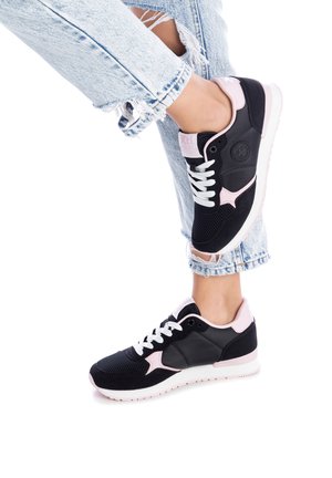 Zapatillas deportivas negras y rosas con parte superior de malla y cuero sintético, cordones blancos y suela texturizada, combinadas con jeans azules desgastados.