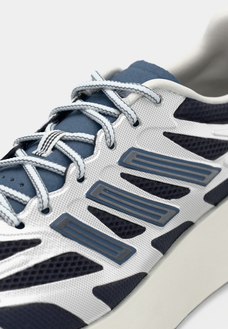 Chaussures de sport dotées d'une tige en maille blanche avec des accents marine foncé, des superpositions grises et des lacets bleu clair. Semelle texturée pour une meilleure adhérence et stabilité.