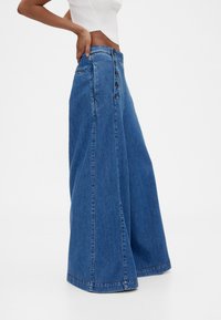 Jeansbyxor med vida ben i en mellanmörkblå tvätt. Har knapplås fram, hög midja och blekt tygstruktur.