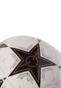 Balón de fútbol blanco con un patrón de estrellas negras, acentos rojos y texto impreso. Hecho de material sintético suave, presenta un acabado brillante.