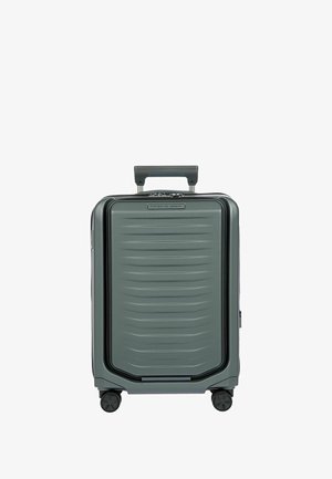 Valise rigide de couleur vert foncé, avec une surface texturée ornée de rainures horizontales, une poignée rétractable et quatre roues pour la mobilité.