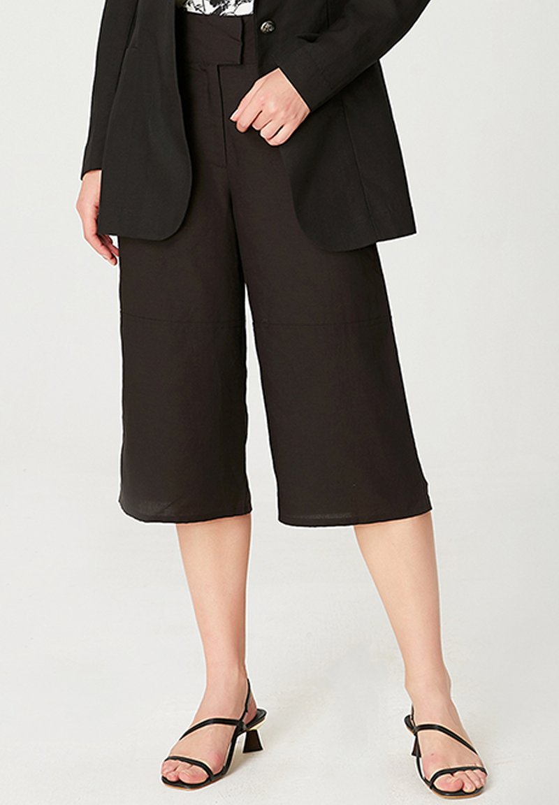 Pantalons noirs raccourcis en tissu léger, avec une coupe décontractée, taille mi-hauteur et texture lisse, associés à des sandales noires à lanières.