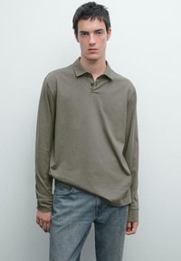 Langarm polo-shirt in olijfgroen katoen, met een kraag, twee knopen voor sluiting, en een comfortabele pasvorm, gecombineerd met lichtgewassen denim jeans.