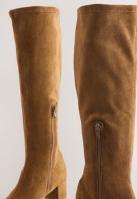 Braune Overknee-Stiefel aus Wildleder mit Blockabsatz. Sie verfügen über zwei seitliche Reißverschlüsse und eine vertikale Nahtführung entlang der Nähte für eine strukturierte Optik.