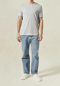 Jasnoszara bawełniana koszulka z krótkim rękawem. Jasnoniebieskie dżinsy o prostym kroju. Białe wsuwane buty o gładkiej powierzchni. Prosty design.