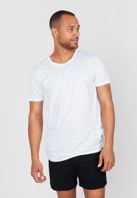 Weißes Baumwoll-T-Shirt mit kurzen Ärmeln und rundem Ausschnitt, kombiniert mit schwarzen Shorts. Glatte Textur, schlichtes Design.