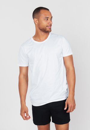 Witte katoenen t-shirt met korte mouwen en een ronde halslijn, gecombineerd met zwarte shorts. Glad textuur, eenvoudig ontwerp.
