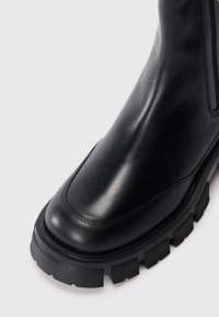 Bota de tornozelo em pele preta com um design elegante, apresentando bico arredondado, sola de borracha texturizada e painéis elásticos laterais para um uso fácil.