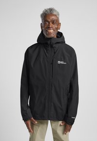 Schwarze wasserdichte Jacke mit Kapuze, Reißverschluss vorne und Logo auf der Brust. Verfügt über eine entspannte Passform und elastische Bündchen. Strukturierter Stoff.