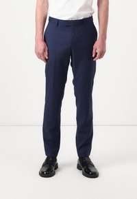 Marineblaue maßgeschneiderte Hose mit schlankem Schnitt, flachem Bund und geraden Beinen, gefertigt aus einem glatten, gewebten Stoff. Schwarze Anzugschuhe vervollständigen das Outfit.