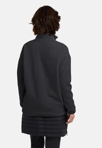 Pullover in pile nero con colletto alto, vestibilità comoda e gonna imbottita a contrasto; presenta una texture liscia e un design a strati.