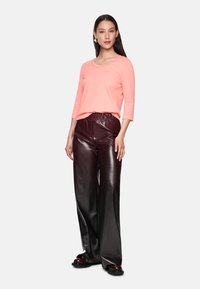 Helles rosa Langarmoberteil mit rundem Halsausschnitt, kombiniert mit glänzenden, dunkelbraunen, weiten Hosen und schwarzen klobigen Schuhen.