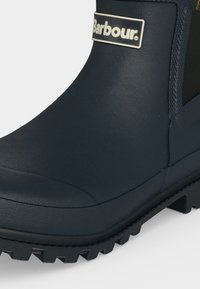 Gros plan d'une botte en caoutchouc noire Barbour avec une semelle texturée et un panneau latéral élastique pour un port facile.