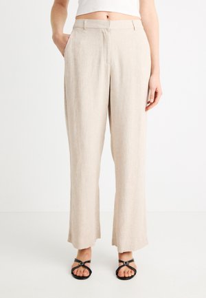 Μπεζ λινό παντελόνι με ίσια γραμμή, με πλαϊνές τσέπες και απαλό ύφασμα. Συνδυασμένο με μαύρα σανδάλια με λουράκια.