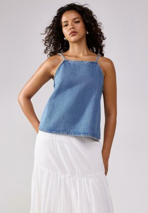 Top in denim blu con spalline sottili, design a taglio dritto e orlo sfrangiato. Abbinato a una maxi gonna bianca a strati e texture.
