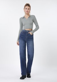 Γκρι μακρυμάνικο cropped τοπ με ριγέ υφή και γιακά, σε συνδυασμό με ψηλόμεσο μπλε τζιν και μαύρα μποτάκια αστραγάλου σε απλό φόντο.