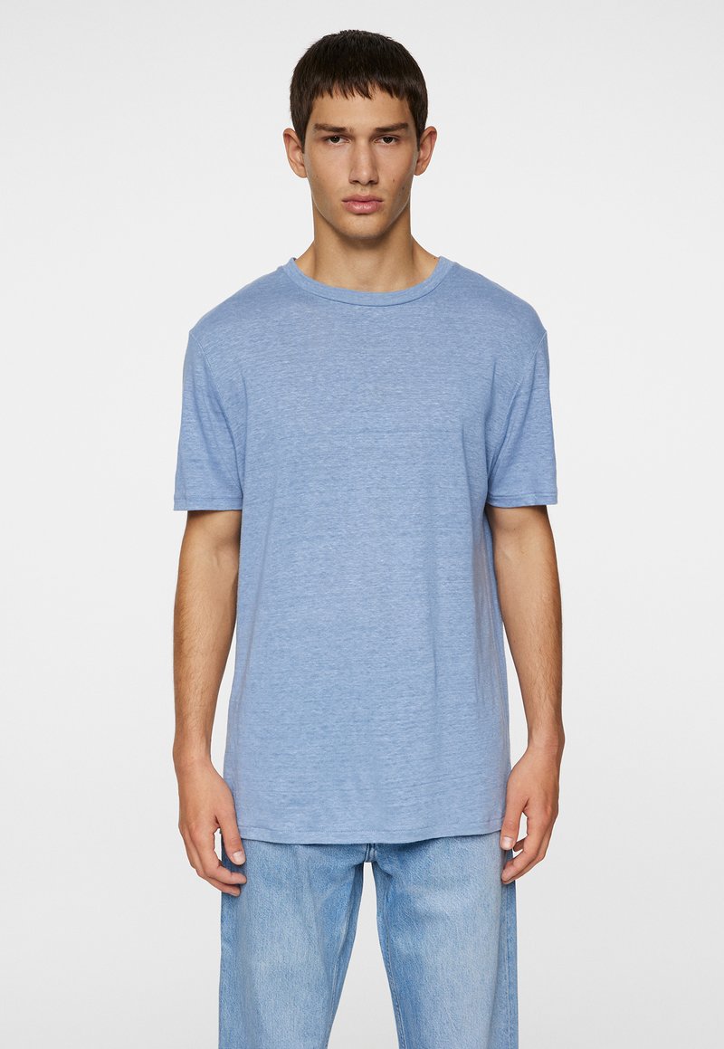 Camiseta de manga corta azul claro en una tela suave y texturada con un escote redondo. Combinada con unos vaqueros de mezclilla claros y holgados.