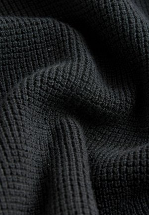 Tissu noir texturé avec un motif en nid d'abeille, présentant des variations subtiles d'épaisseur et une surface douce, légèrement duveteuse.