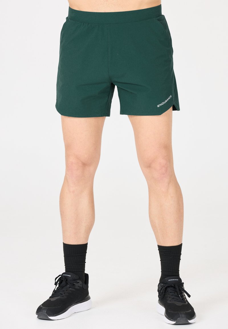 Grüne Sportshorts mit elastischem Bund, Seitentaschen und gesticktem "ENDURANCE"-Logo auf der unteren rechten Seite.
