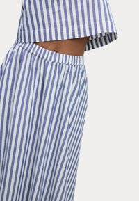 Completo a due pezzi a strisce blu e bianche composto da un top corto morbido e pantaloni con vita elastica, realizzato in tessuto leggero con una consistenza soffice.