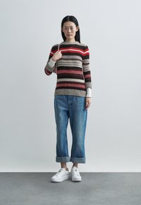 Pull rayé beige, rouge et marron, à manches longues et ourlet côtelé, associé à un jean en denim retroussé et des baskets blanches.