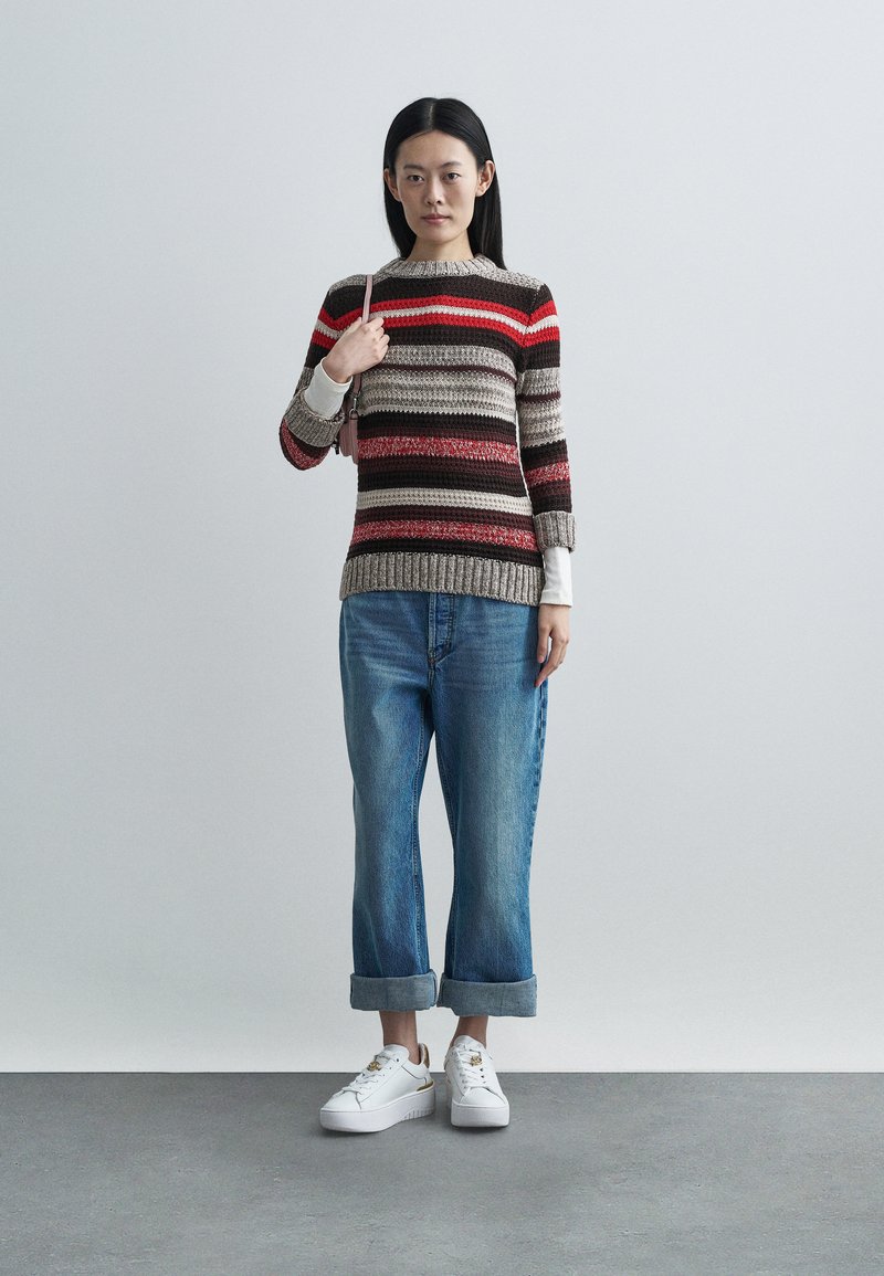 Pull rayé beige, rouge et marron, à manches longues et ourlet côtelé, associé à un jean en denim retroussé et des baskets blanches.