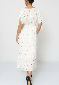 Robe blanche à manches courtes, ornée de broderies florales dorées, avec une taille cintrée et un ourlet à volants. Fabriquée dans un tissu léger au toucher fluide.