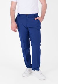 Pantaloni blu su misura con una texture liscia, dotati di tasche laterali, chiusura con bottone, abbinati a sneaker bianche.