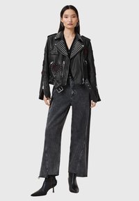 Black leather biker jacket with silver studs, patches, and zippers; paired with high-waisted, straight-leg gray denim jeans and black ankle boots.