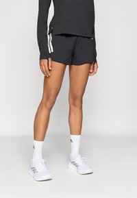 Čierne športové šortky so šnúrkou v páse, v kombinácii s čiernym dlhým rukávom. Biele športové topánky so sivými a ružovými detailmi.