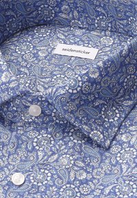 Tessuto blu a pattern con design floreali e paisley bianchi. Presenta una trama intrecciata e un'etichetta bianca contrassegnata "seidensticker" con bottoni.