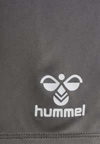 Szary materiał o gładkiej strukturze z wyraźnym białym logo i emblematem "hummel" na dole. Prosty design, bez dodatkowych wzorów.