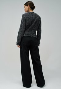 Pantalons larges noirs associés à un pull gris texturé. Le pull a des bords effilochés et des manches longues, mettant en avant une silhouette décontractée et superposée.