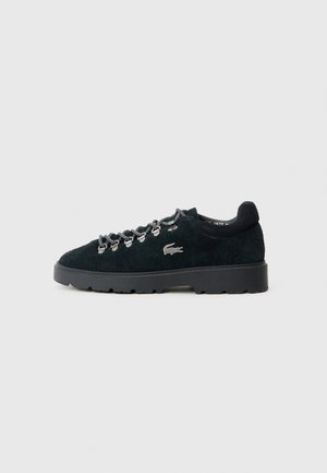 Czarny zamszowy sneaker z grubą podeszwą, metalowymi oczkami, czarno-białymi sznurowadłami i srebrnym logo krokodyla z boku.