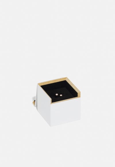 Hvid smykkeæske med en guldtrimmet top, der har et sort fløjlindhold, som holder to små øreringe. Firkantet form med et minimalistisk design.