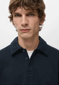 Granatowy t-shirt polo z klasycznym kołnierzykiem i trzypunktowym zapięciem na guziki. Miękka faktura tkaniny z czystym, minimalistycznym wzornictwem.