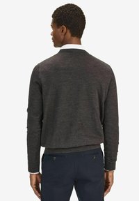 Mörkgrå stickad tröja med rundad halsringning, åtsittande muddar och en fåll som når vid midjan. Bärs över mörka byxor med fickor.