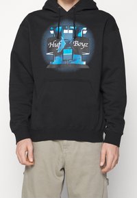 Sudadera negra con capucha que presenta un gráfico frontal con acentos en azul y el texto "Huf Boyz", confeccionada en una suave tela texturizada y con un bolsillo tipo canguro.