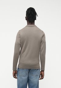 Szary sweter z długim rękawem o teksturowanym splocie, z okrągłym dekoltem i ściągaczami przy mankietach, zestawiony z jasnoniebieskimi, luźnymi dżinsami.