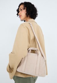 Beige corduroy handbag with dual top handles and a long adjustable strap. Rounded shape with textured surface and silver zipper accents.