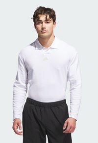 Vit långärmad polo med klassisk krage och liten beige logotyp. Bärs med svarta byxor med elastisk midja som erbjuder en figurnära design.