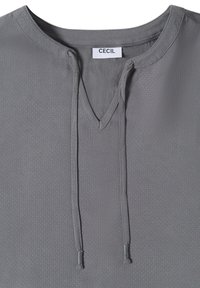 Blouse en tissu gris texturé avec col en V et liens à nouer, étiquette "CECIL" à l'intérieur du col.