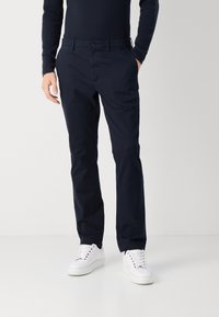 Chino blu navy realizzati in tessuto misto cotone, con un design a gamba dritta, tasche anteriori e chiusura con un solo bottone. Indossati con sneaker bianche.