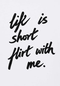 Texte brodé en noir sur tissu blanc : « la vie est courte, flirte avec moi » en écriture cursive décontractée.