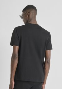 Camiseta de algodón negra con un corte clásico. Mangas cortas, cuello redondo, textura suave y sin patrones ni gráficos visibles.