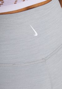 Leggings atletici grigio chiaro realizzati in un tessuto elastico, con un logo Nike bianco sulla vita e sottili strisce testurizzate.