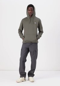 Felpa a cappuccio verde oliva con tasca a marsupio e coulisse, abbinata a pantaloni cargo grigi con tasche laterali e vestibilità relaxed.