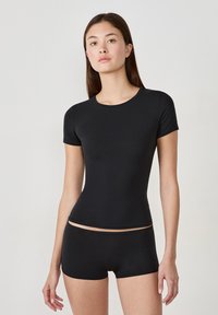 Top ajustado de manga corta negro hecho de una tela suave con escote redondo, combinado con parte inferior tipo braga negra a juego.